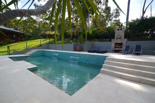 Backyard swimming pool with steps, turquoise water, palm trees, and a patio with lounge chairs