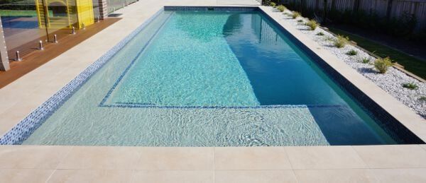 Rectangular outdoor pool with blue water and a narrow swimming lane, bordered by a stone deck and plants