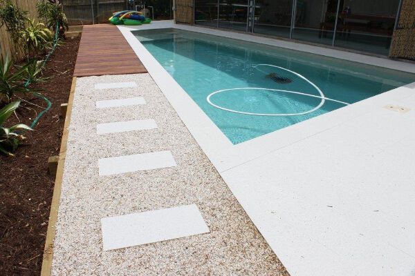 Modern outdoor pool with a pebble walkway and white stepping stones beside turquoise water