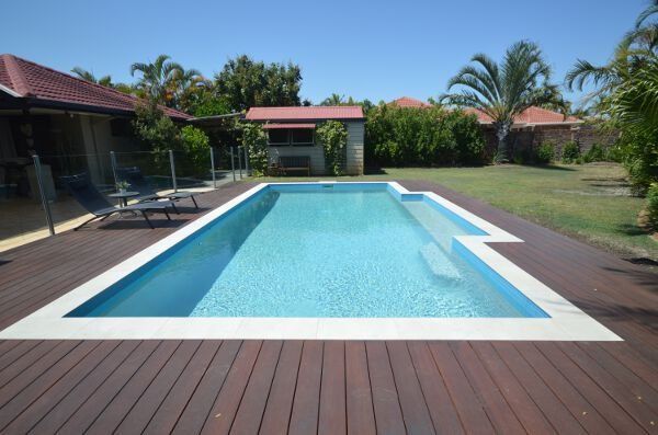 Backyard swimming pool with clear blue water, wooden deck, and tropical landscaping