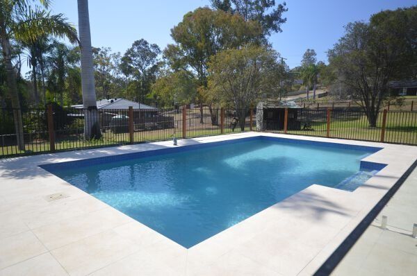 Backyard swimming pool with light blue water and a fenced yard with trees in the background