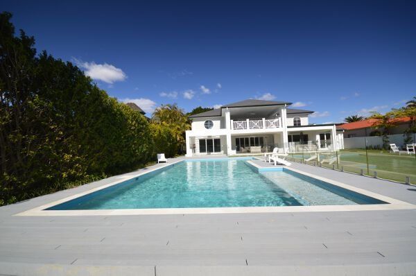 Modern white house with a large turquoise swimming pool and deck under a clear blue sky