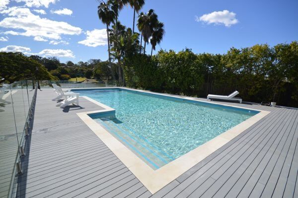 Modern backyard pool with turquoise water, gray deck, lounge chairs, and palm trees under a blue sky