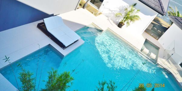 Modern blue swimming pool with lounge chairs and white building in bright sunlight