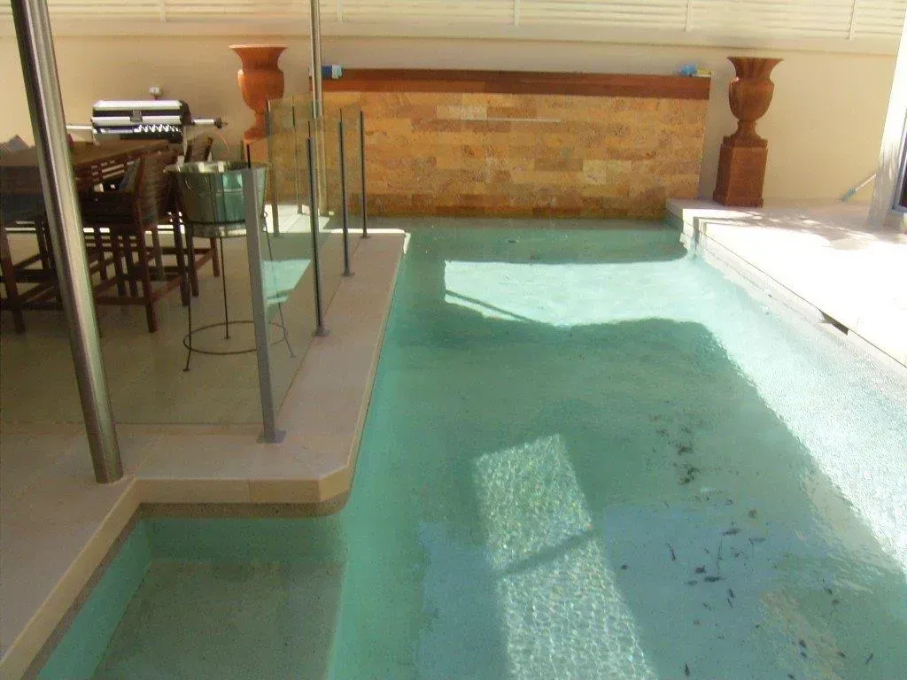 Indoor swimming pool with turquoise water, a raised hot tub edge, and patio furniture nearby