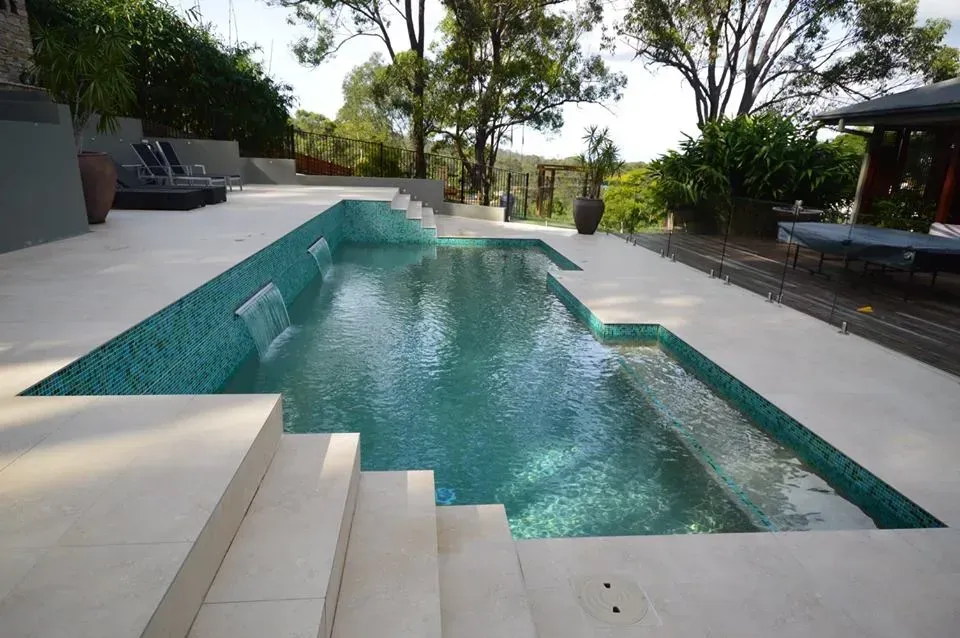 Modern backyard pool with turquoise water, white decking, steps, and surrounding trees