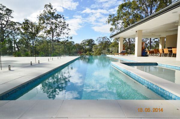 Modern backyard with a long swimming pool, white patio, and a covered seating area under a blue sky