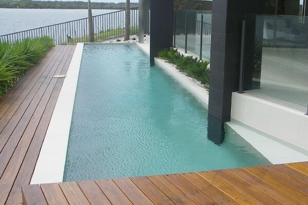 Modern patio with narrow turquoise reflecting pool beside wood deck and glass-fronted house