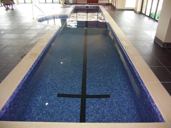 Indoor lap pool with blue tiled water lane and a black cross marker at the near end