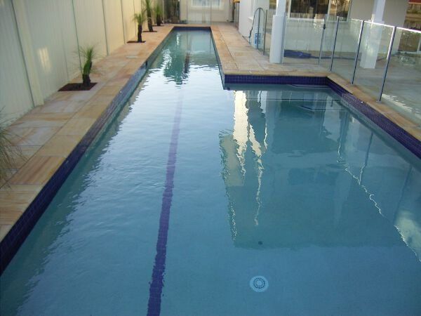 Indoor swimming pool with clear blue water and a shallow ledge beside glass walls