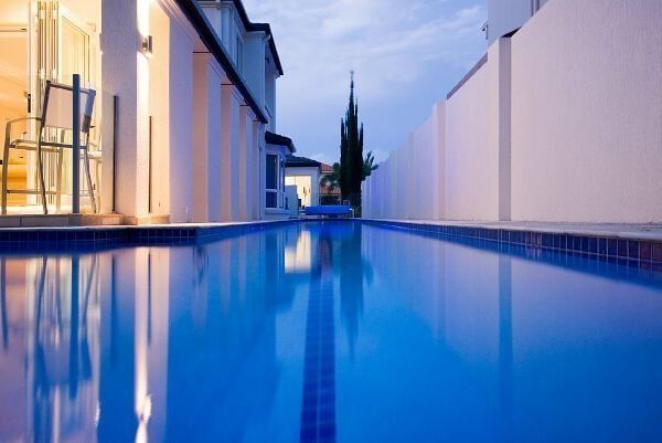 Modern backyard pool beside contemporary houses at dusk, with blue water reflecting the evening sky