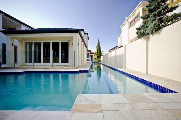 Modern backyard pool with white stone deck and villa-style homes reflected in calm blue water
