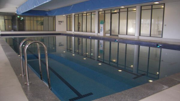 Indoor swimming pool with blue water, metal ladder, and large windows along one side
