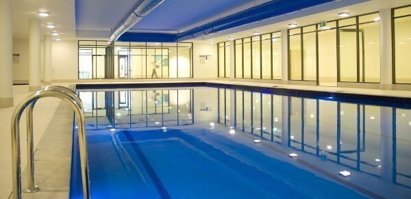 Indoor swimming pool with blue water, lane lines, and large windows reflecting lights