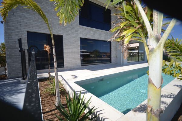 Modern house courtyard with a rectangular pool, palm trees, and dark brick walls