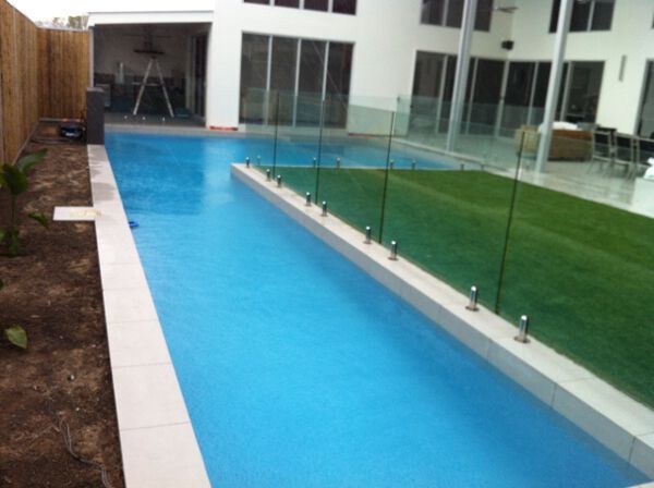 Narrow blue courtyard pool beside a glass wall and green lawn in a modern building courtyard