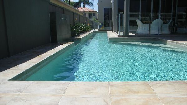 Modern backyard swimming pool with blue water beside a house and patio.
