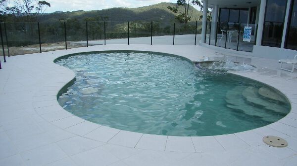Outdoor kidney-shaped pool with clear water on a tiled patio, overlooking hills and a fence