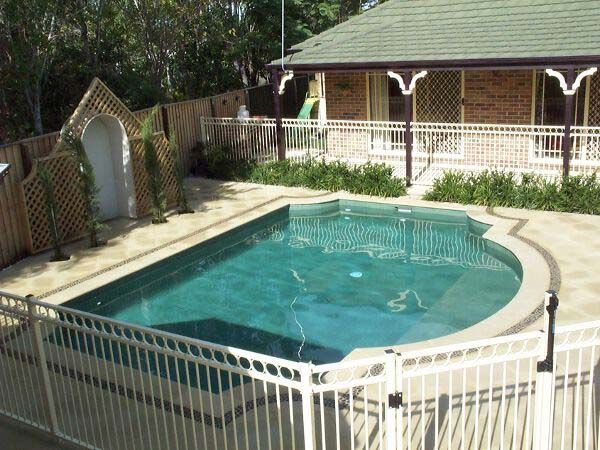 Backyard swimming pool with white fence, stone deck, and house in the background