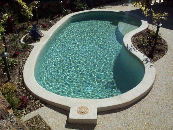 Curved backyard swimming pool with turquoise water, white coping, and surrounding gravel landscaping