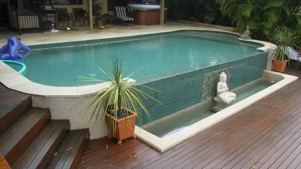 Small backyard pool with turquoise water, wood deck, potted plant, and white statue by the edge