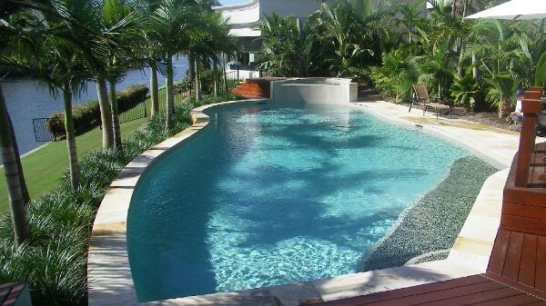 Curved outdoor swimming pool lined with palm trees, blue water, and a tropical resort walkway.