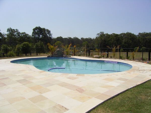 Outdoor swimming pool with pale stone deck and trees in the background