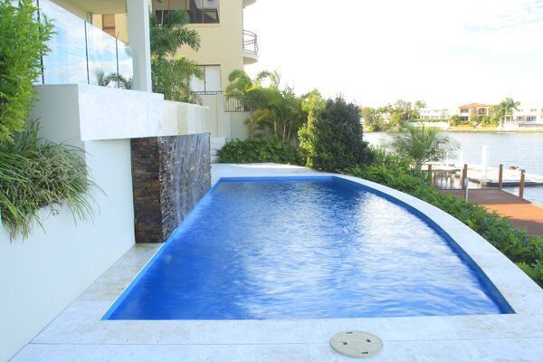Outdoor infinity pool beside modern white building, with blue water and waterfront view
