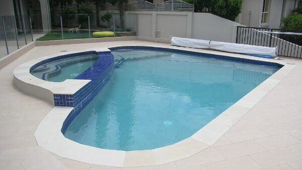 Blue swimming pool with white deck and a raised spa beside a fence and house patio