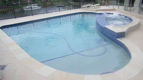 Small backyard swimming pool with a curved spa and light blue water beside a tiled deck