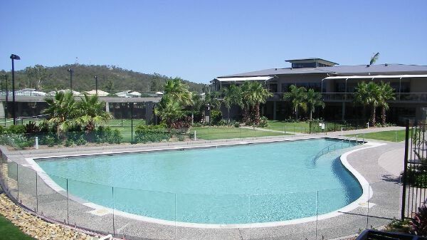 Curved outdoor swimming pool beside a landscaped resort building under a clear sky