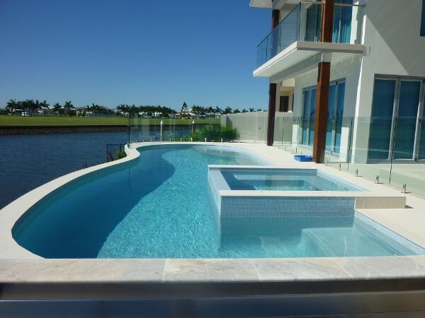 Modern white house with a curved blue swimming pool beside a waterfront view