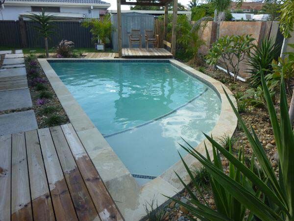 Backyard swimming pool with curved edge, wooden deck, and tropical landscaping