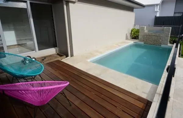 Modern backyard deck with a small rectangular pool and two colorful lounge chairs