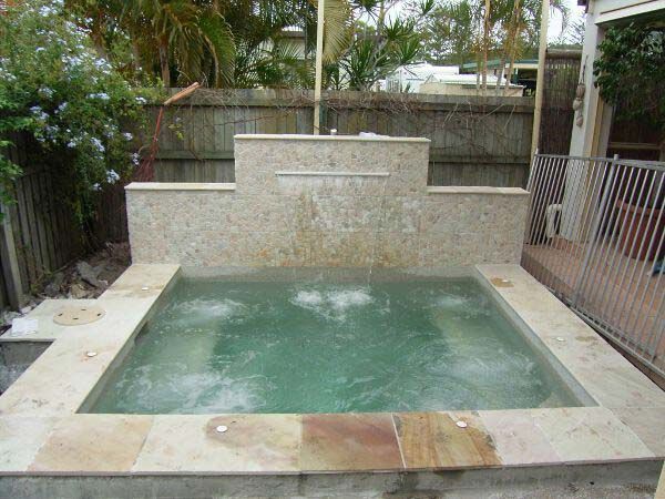 Small outdoor hot tub with bubbling water, stone surround, and plants in a patio setting