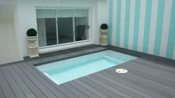 Modern indoor pool deck with a small rectangular pool, gray flooring, and teal striped walls