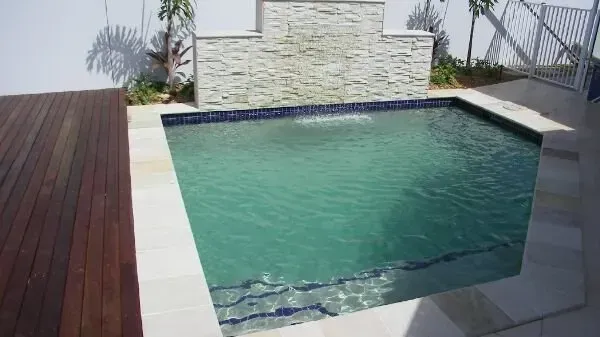 Small rectangular backyard pool with turquoise water and stone wall backdrop