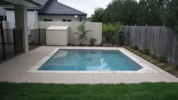 Backyard swimming pool with blue water, bordered by white tile and surrounded by grass and fencing