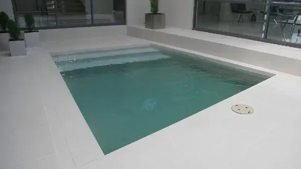 Indoor rectangular pool with turquoise water, white deck, and large windows in a modern room