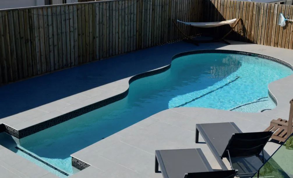 Backyard swimming pool with blue water, lounge chairs, and a fenced deck in sunlight