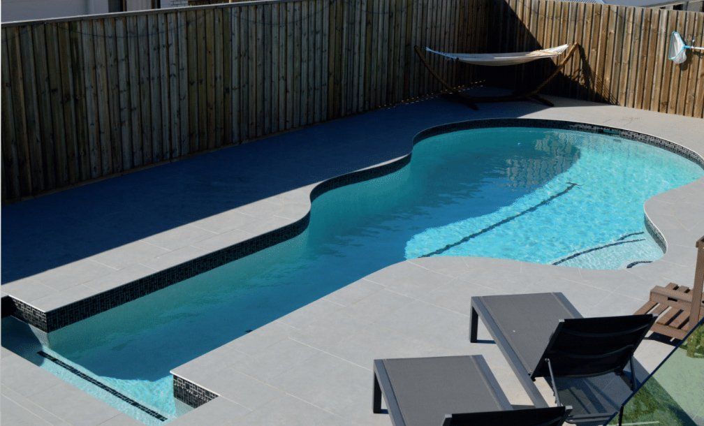 Modern backyard pool with blue water, white deck, lounge chairs, and a hammock by a wooden fence
