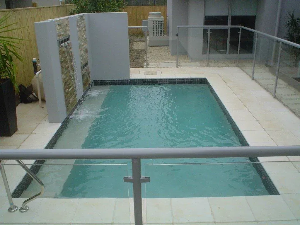Modern courtyard pool with turquoise water, white tile deck, glass railing, and white privacy walls
