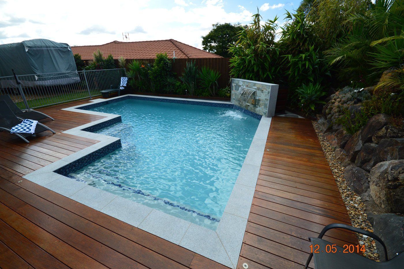 Backyard swimming pool with blue water, surrounded by wooden deck and stone landscaping.