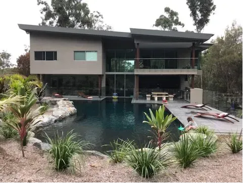 Modern two-story house with a large backyard pool and tropical landscaping