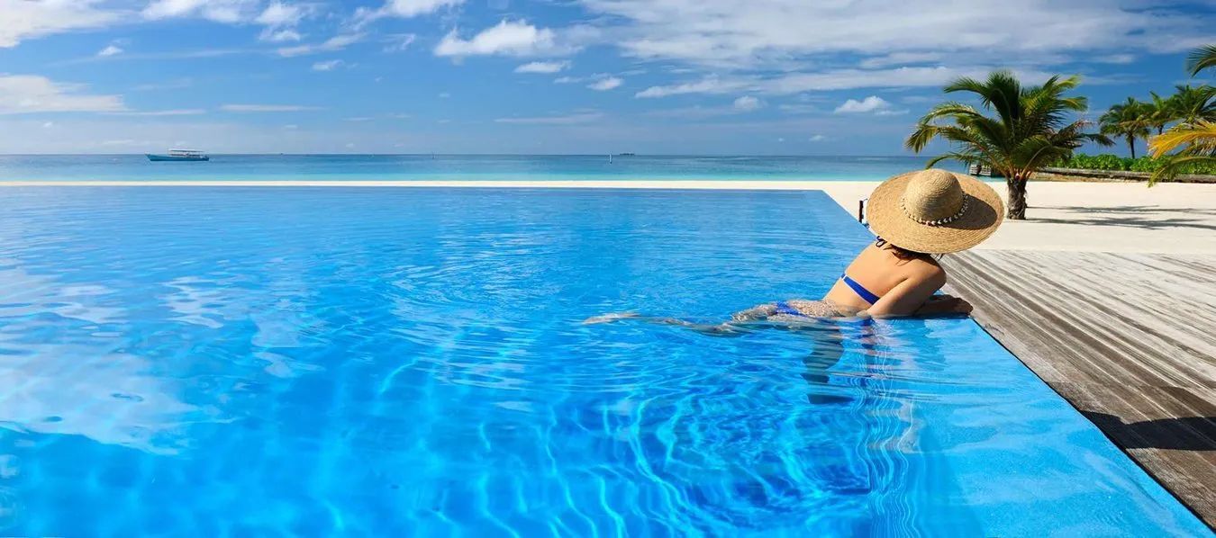 Woman relaxing by an infinity pool overlooking a bright blue ocean and sky