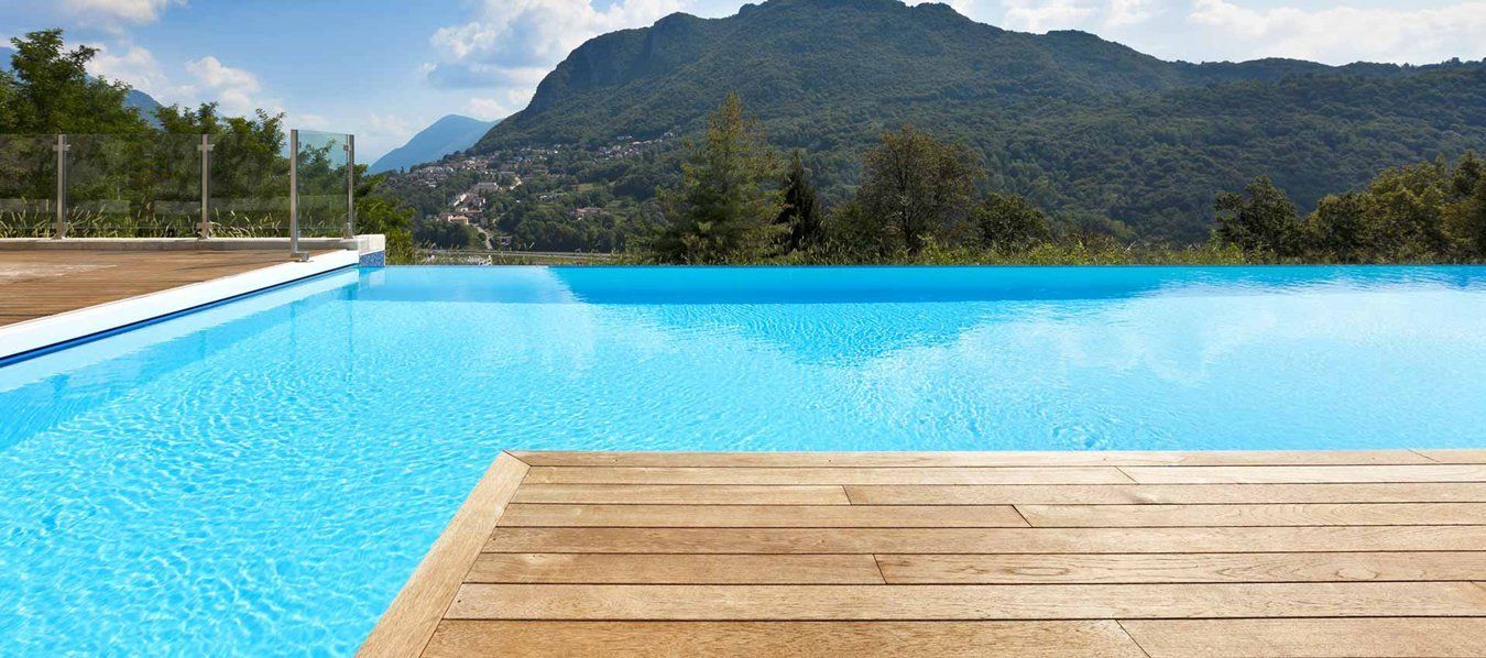Infinity pool with bright blue water, wooden deck, and mountains under a clear sky