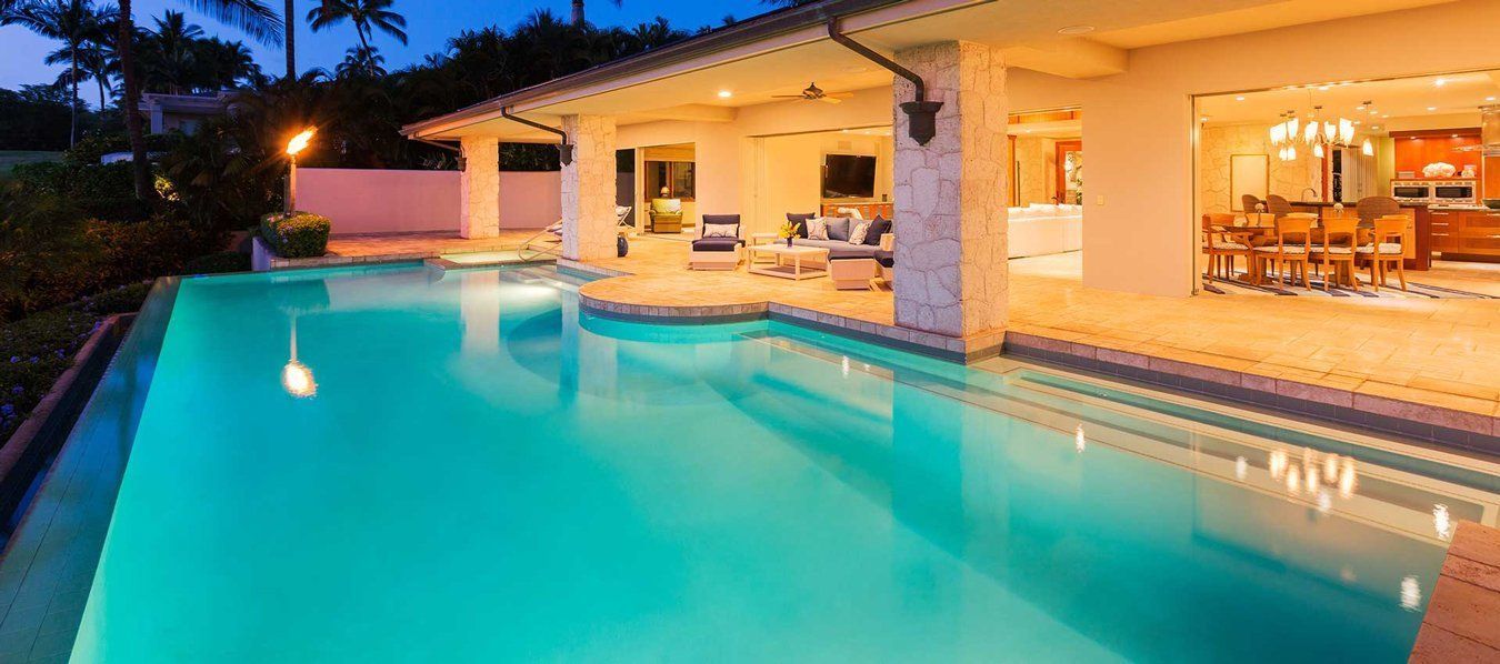 Luxury backyard pool beside a modern house at dusk, with warm interior lights and turquoise water