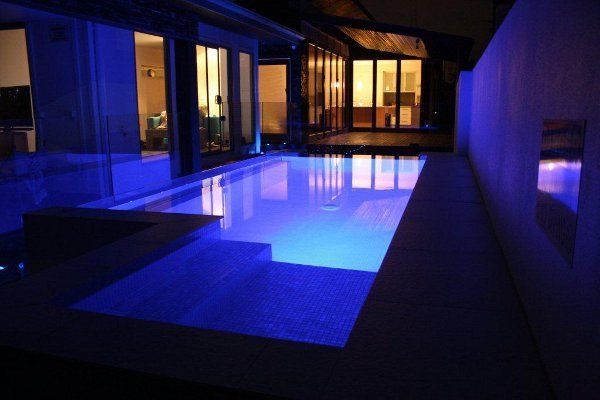 Modern house patio with a glowing blue-lit swimming pool at night
