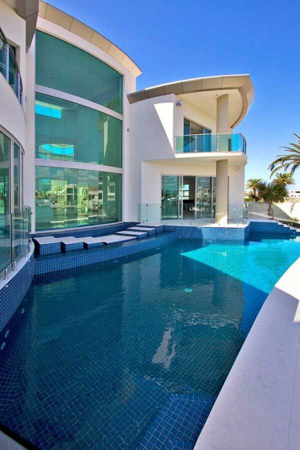 Modern luxury villa with turquoise pool, curved glass windows, and ocean view