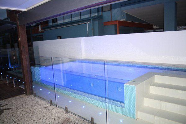 Modern indoor pool with blue water, glass railing, and white stairs at night